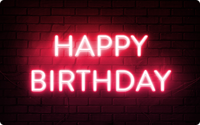 Eine Gutscheinkarte zeigt den Schriftzug 'HAPPY BIRTHDAY' in leuchtend roten Neonbuchstaben vor einem schwarzen Ziegelmauer-Hintergrund.