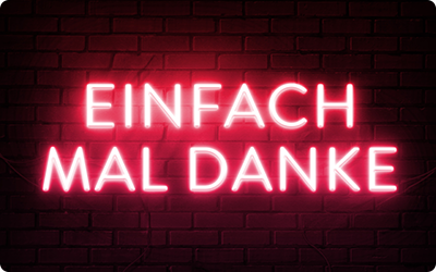Eine Gutscheinkarte zeigt den Schriftzug 'Einfach mal Danke' in leuchtend roten Neon-Großbuchstaben vor einem schwarzen Ziegelmauer-Hintergrund.