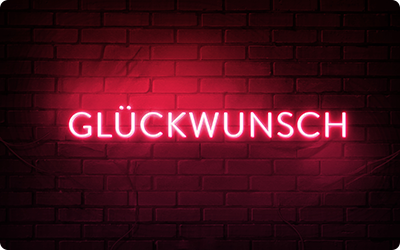 Eine Gutscheinkarte zeigt den Schriftzug 'Glückwunsch' in leuchtend roten Neon-Großbuchstaben vor einem schwarzen Ziegelmauer-Hintergrund.